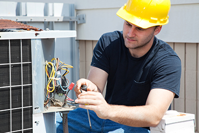 A repairman looking at an AC blower inside an AC unit.