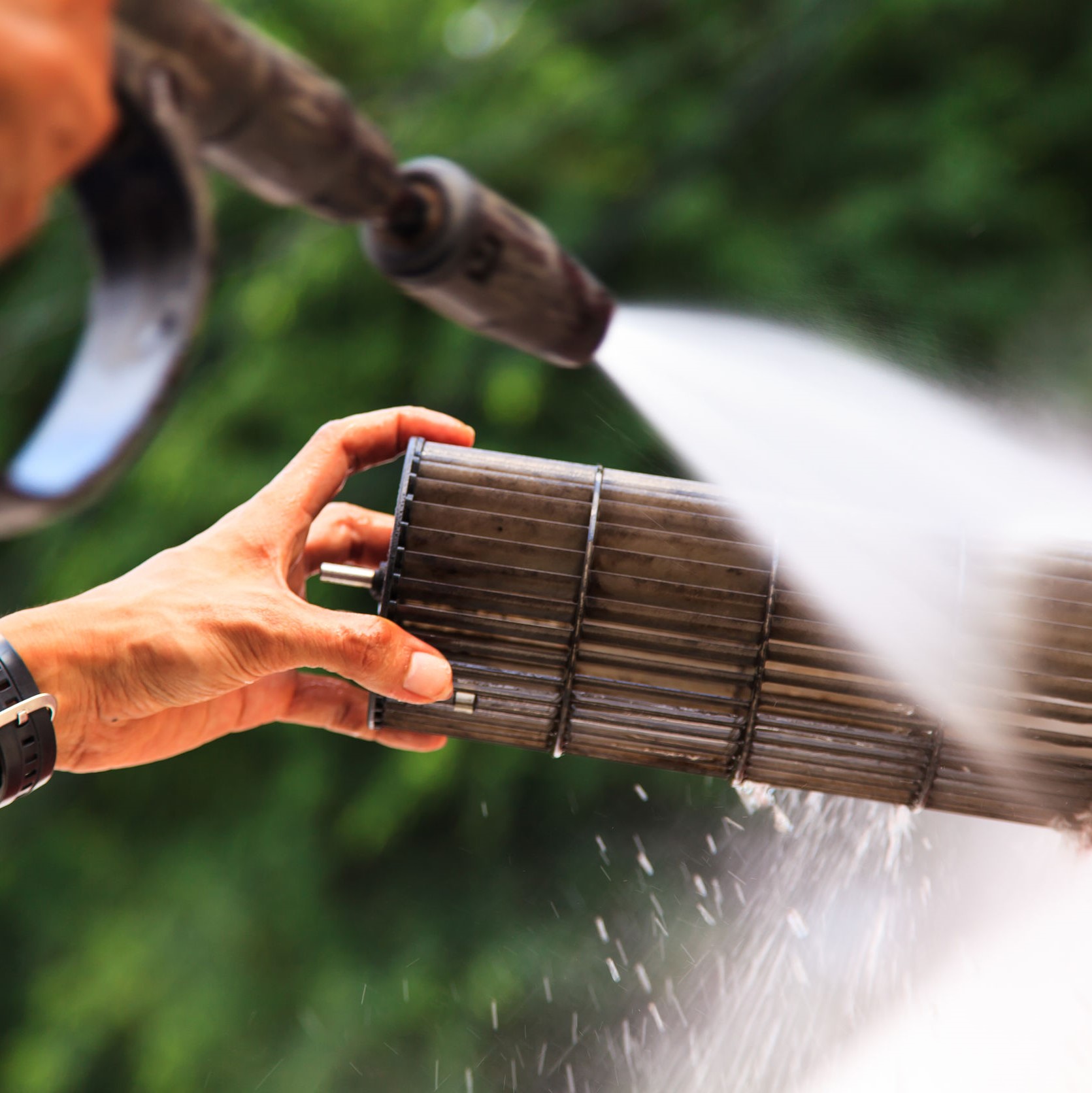 A worker cleaning out part of an AC unit with a pressure washer nozzle.