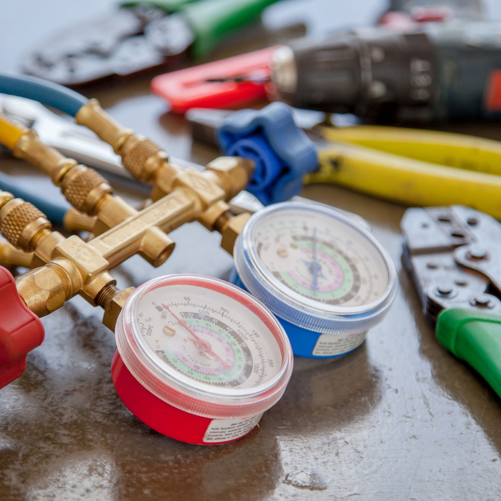 Tools to fix an air conditioner laid out on the table. There are wire cutters, a drill, and a pressure gauge.