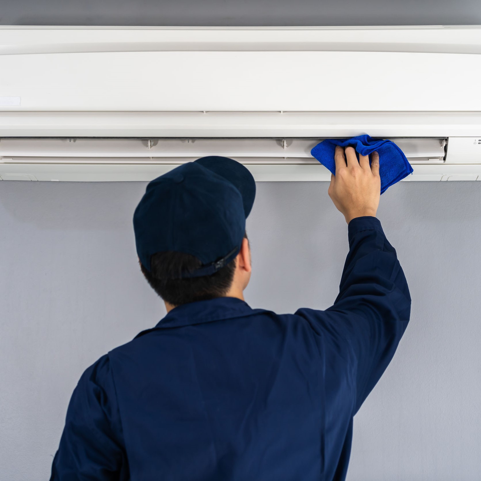 A repairman cleaning an indoor AC unit.