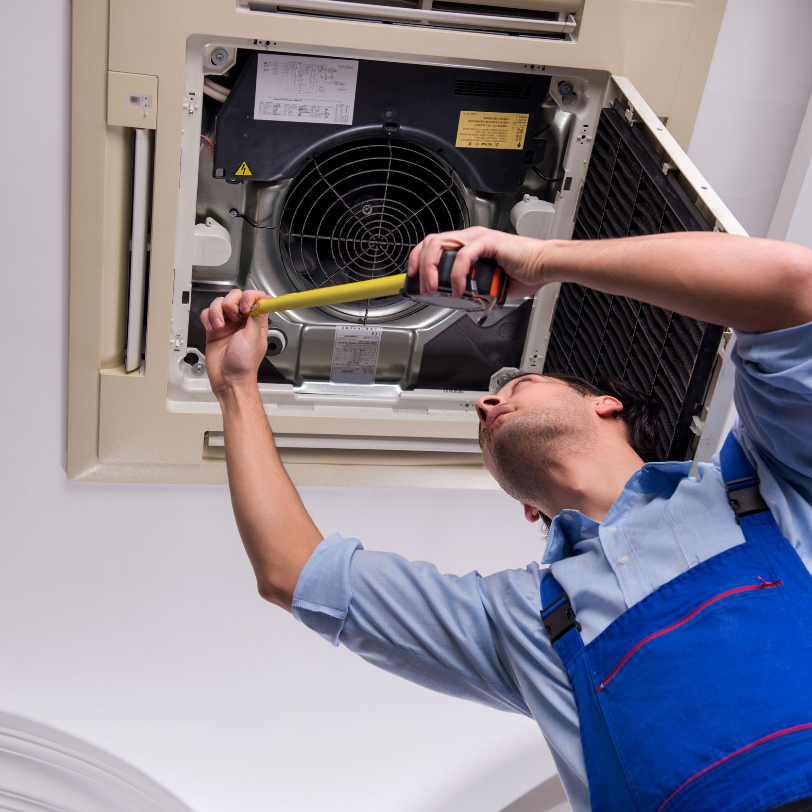 A repairman fixing an HVAC unit on the ceiling. 