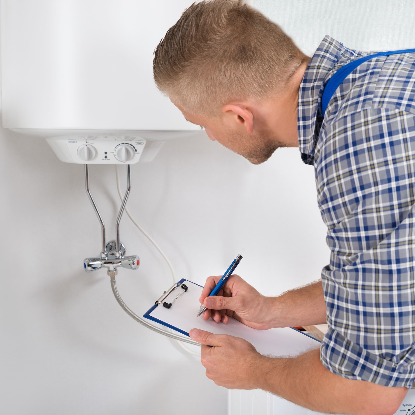 A worker looking at a heater and writing on a clipboard.