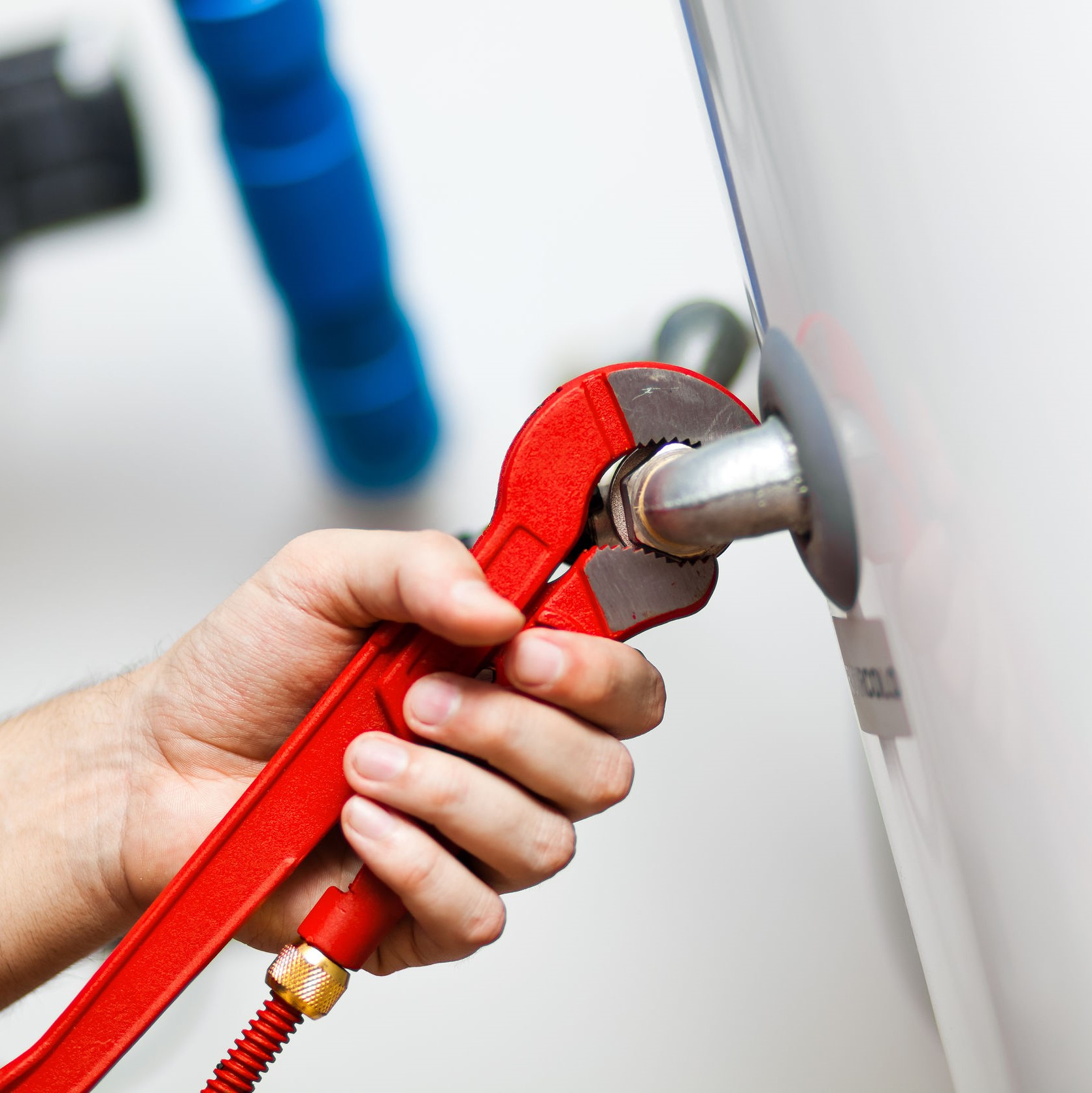 A repairman holding a red wrench on a water heater. 